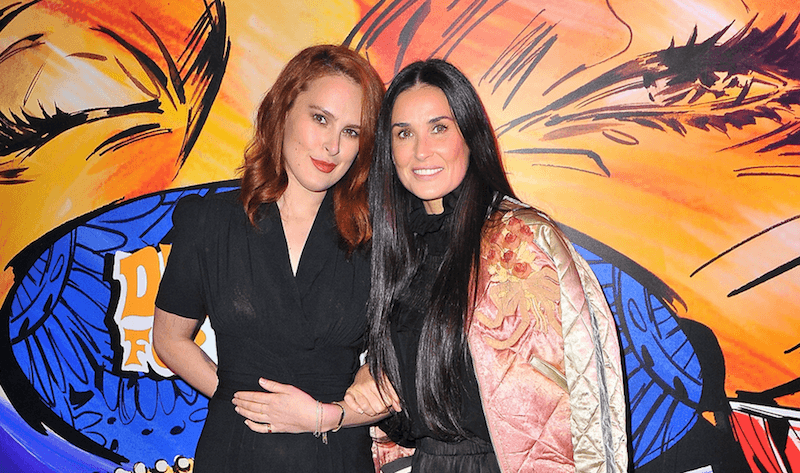 Rumor Willis and Demi Moore posing in front of a colorful background at a premiere. 
