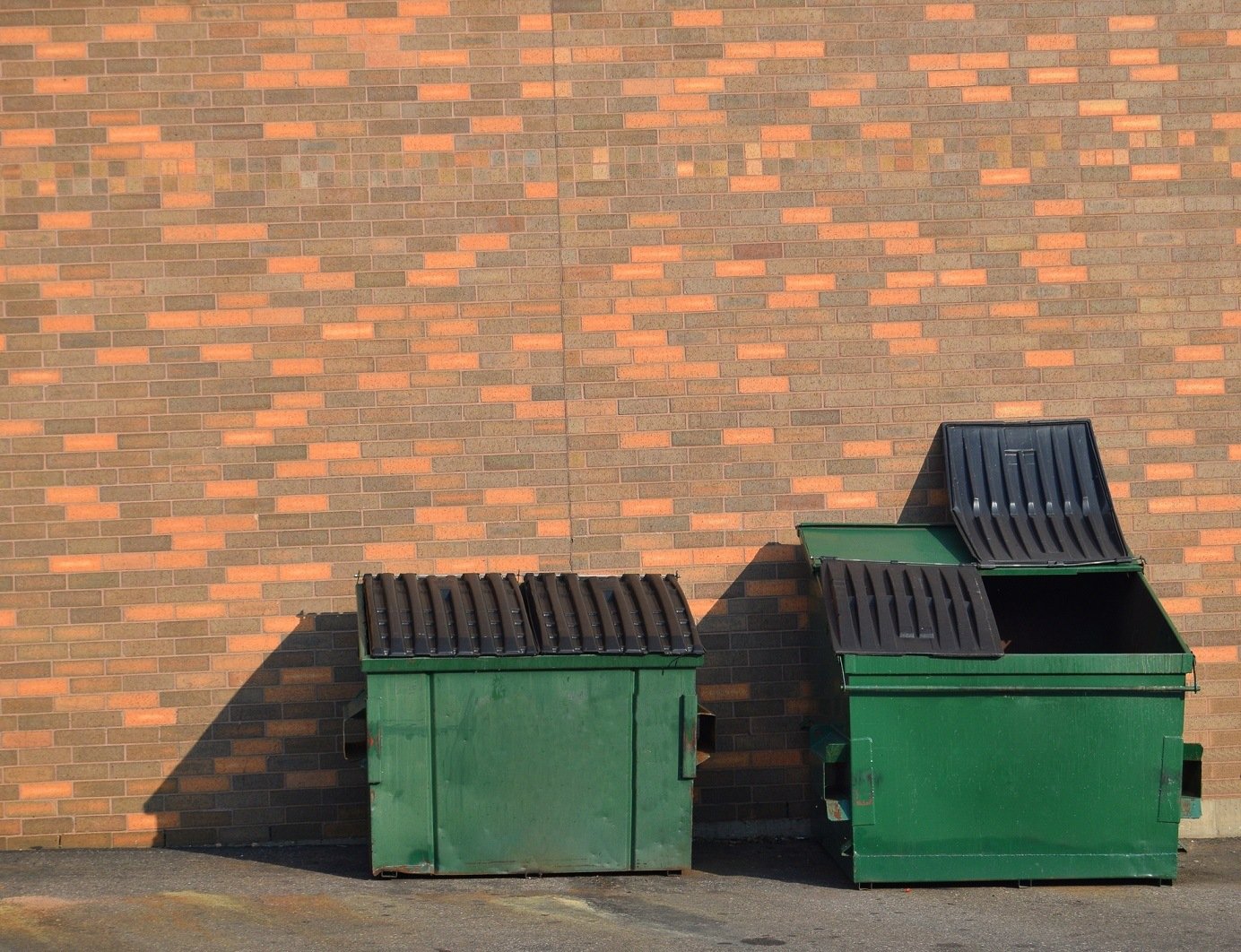 Green recycling dumpsters against a brick wall