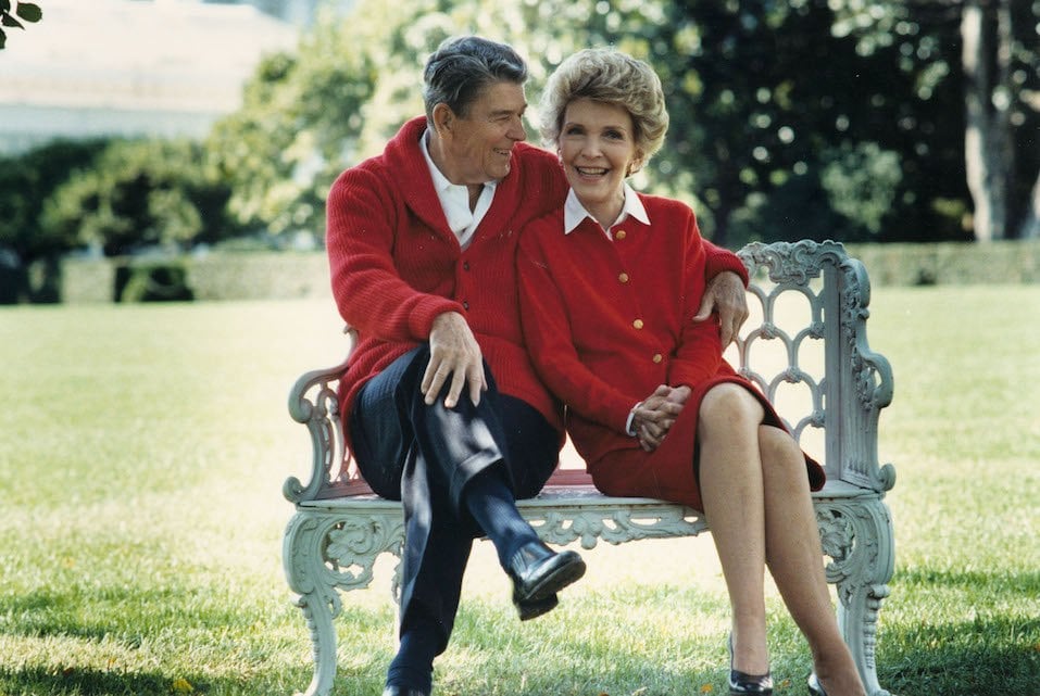 U.S. President Ronald Reagan and First Lady Nancy Reagan sit on a bench in matching red sweaters. 
