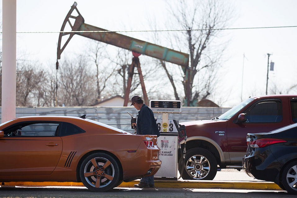 A motorist fills his car with gas at a gas station near an oil field pumping rig
