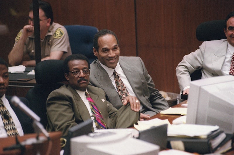 LOS ANGELES, CA - MARCH 22: Murder defendant O.J. Simpson (C-R), seated next to his lawyer Johnnie Cochran, Jr. (C-L), smiles as witness Brian "Kato" Kaelin testifies about acting job offers he has gotten as a result of publicity surrounding the night of the murders, during the O.J. Simpson double-murder criminal trial on March 22, 1995 in Los Angeles, California. The murder case is being televised internationally, due to global interest in the case where former American Football star and film actor O.J. Simpson has been charged with the stabbing murder of his former wife, Nicole Brown Simpson, and her friend Ronald Goldman. (Photo credit should read VINCE BUCCI/AFP/Getty Images) *** Local Caption *** O.J. Simpson;Johnnie Cochran