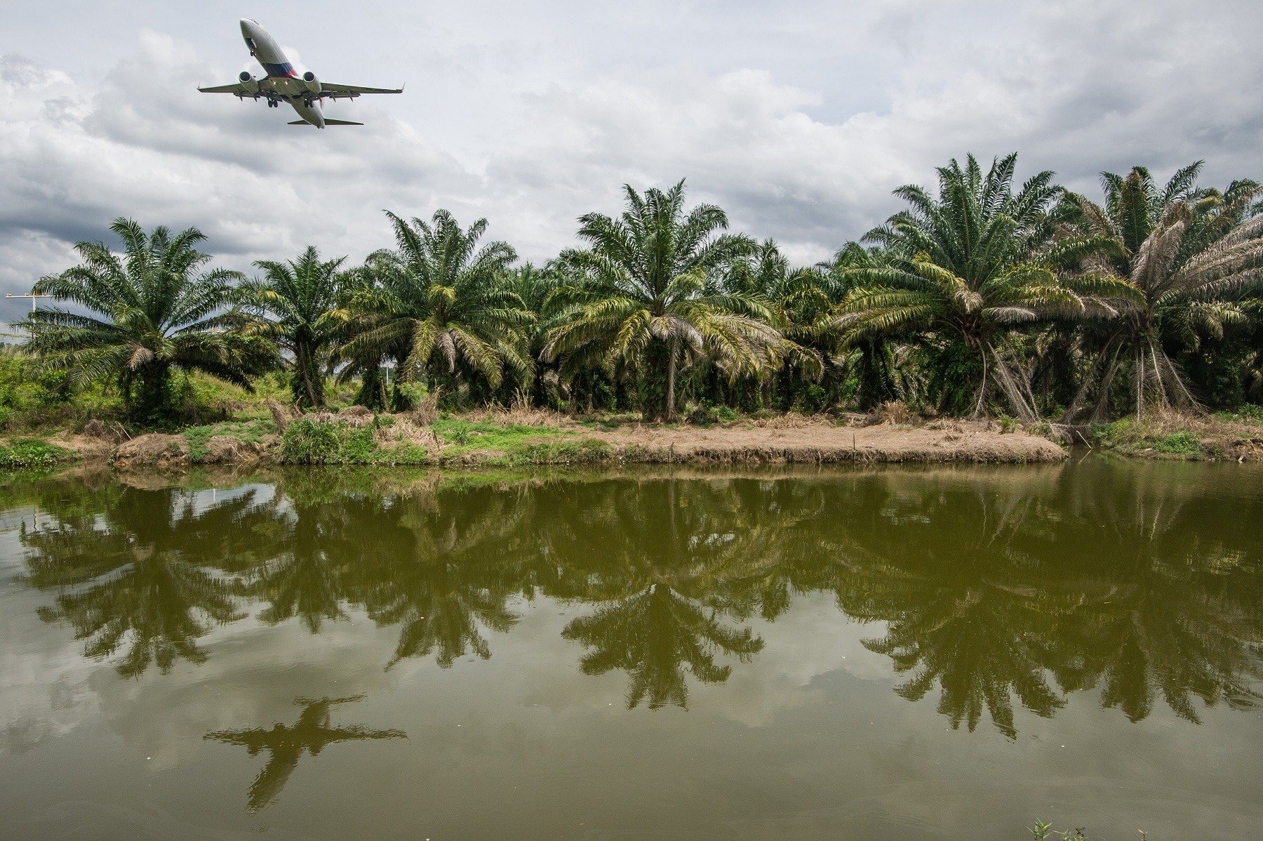 A Malaysia Airlines plane (L) is reflected as it flies over a river
