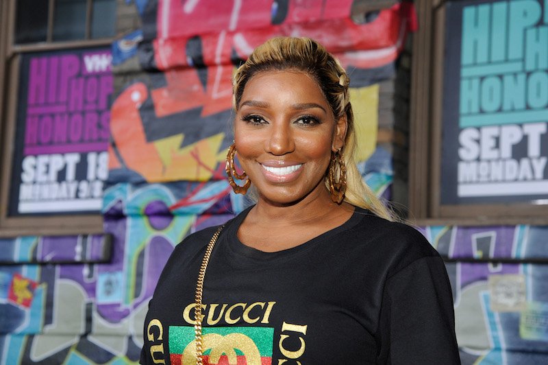 NeNe Leakes smiling while standing in front of a colorful background of posters and street art.