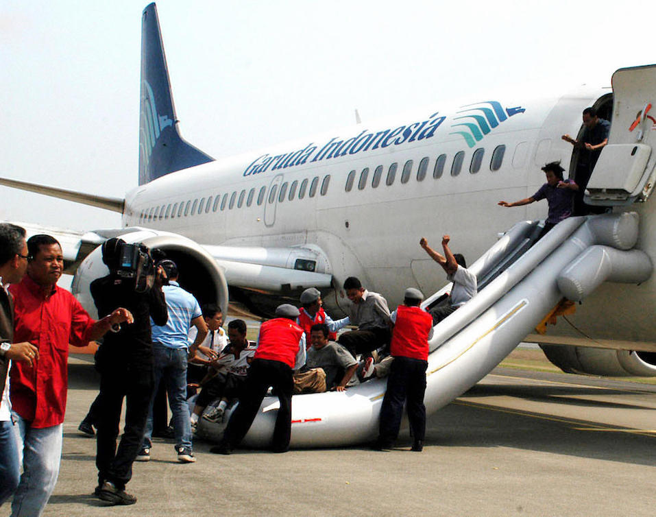 People acting as passengers slide through an emergency chute
