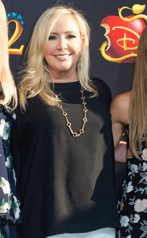 Shannon posing on a red carpet in a black shirt and white pants. 