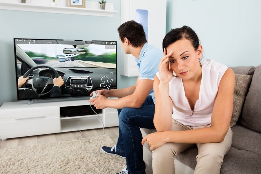 Man playing a video game while a woman sits next to him looking upset Man playing a video game while a woman sits next to him looking upset