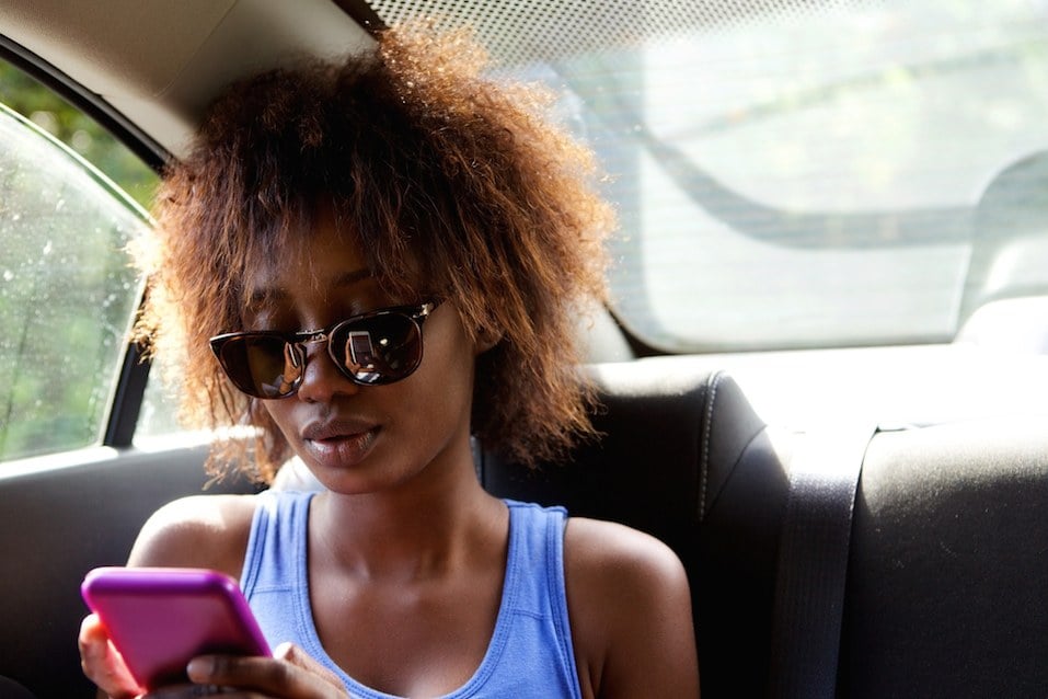 Woman sitting in backseat of car looking at cell phone