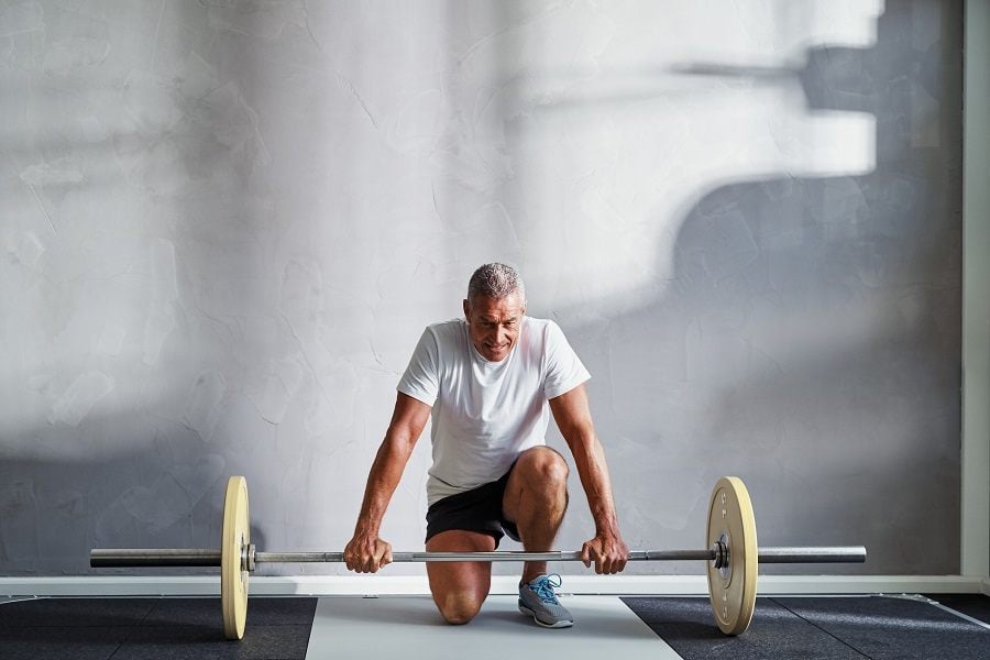 senior man in sportswear kneeling alone in a gym