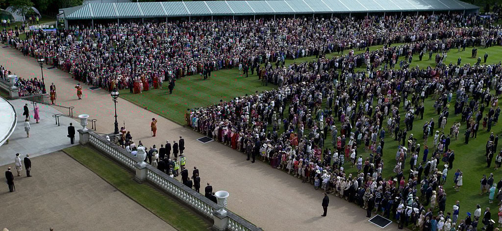 Queen Elizabeth II (wearing pink) stands with Prince Philip, Duke of Edinburgh on the top of the steps in front of members of the public