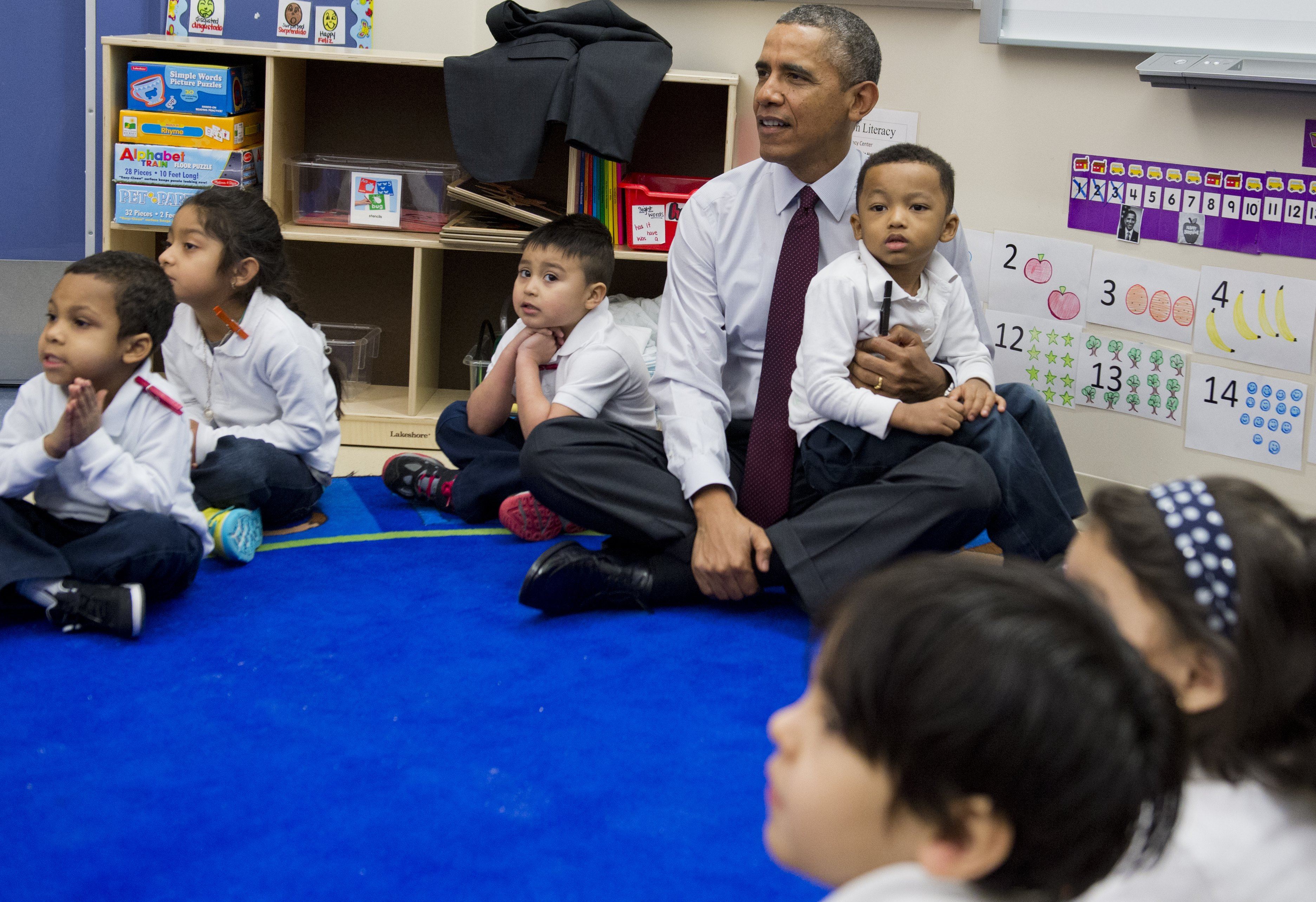 Barack Obama sits cross legged on the floor and holds a child in his lap