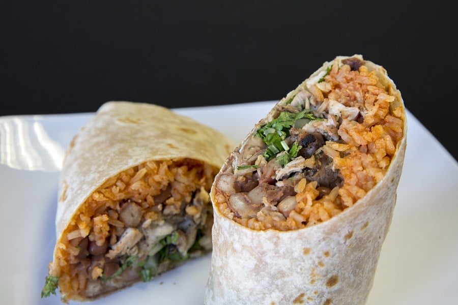 Tow halves of a burrito with rice, beans, and steak on a white plate
