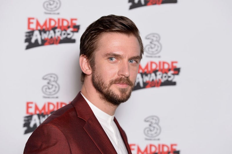 Dan Stevens wears a red blazer while on a red carpet. 