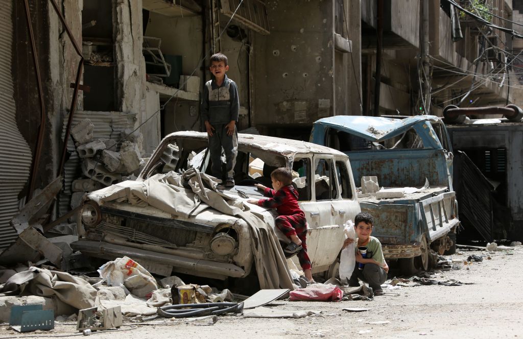 Syrian boys play on a destroyed car in the former rebel-held Syrian town of Douma