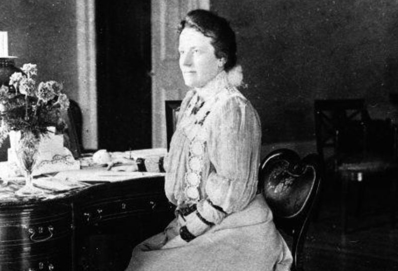 Edith Roosevelt sitting at a desk decorated with flowers. 