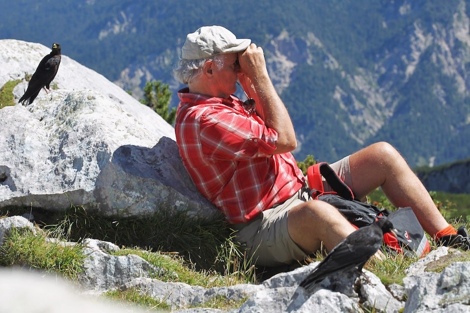A elder male tourist looks out with field glasses