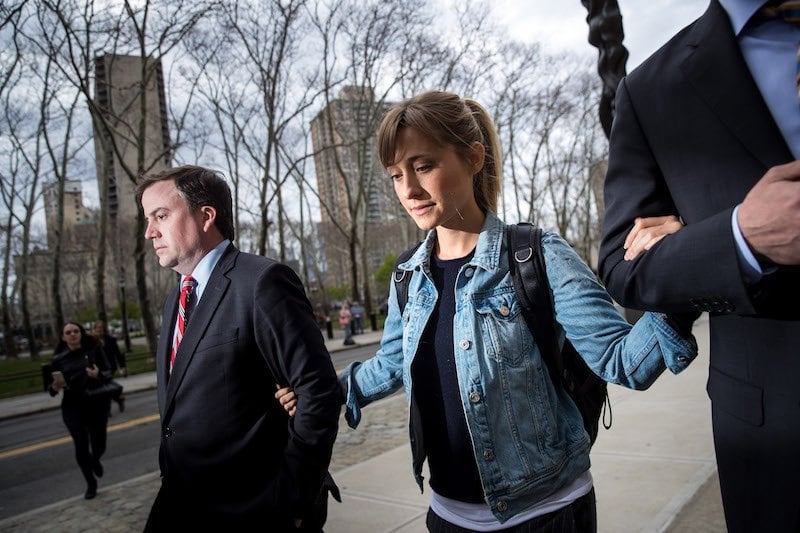 Allison Mack holds on to the arms of her two lawyers