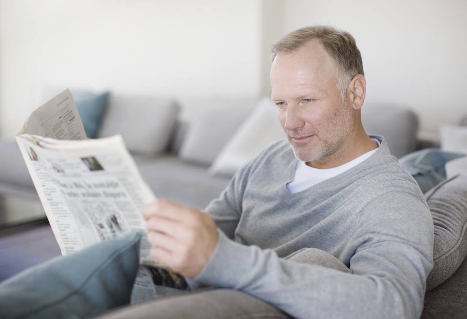 Man sitting on sofa reading newspaper