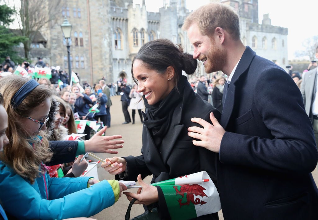 Meghan Markle writes a note for 10 year old Caitlin Clarke from Marlborough Primary School as Prince Harry looks on during a walkabout