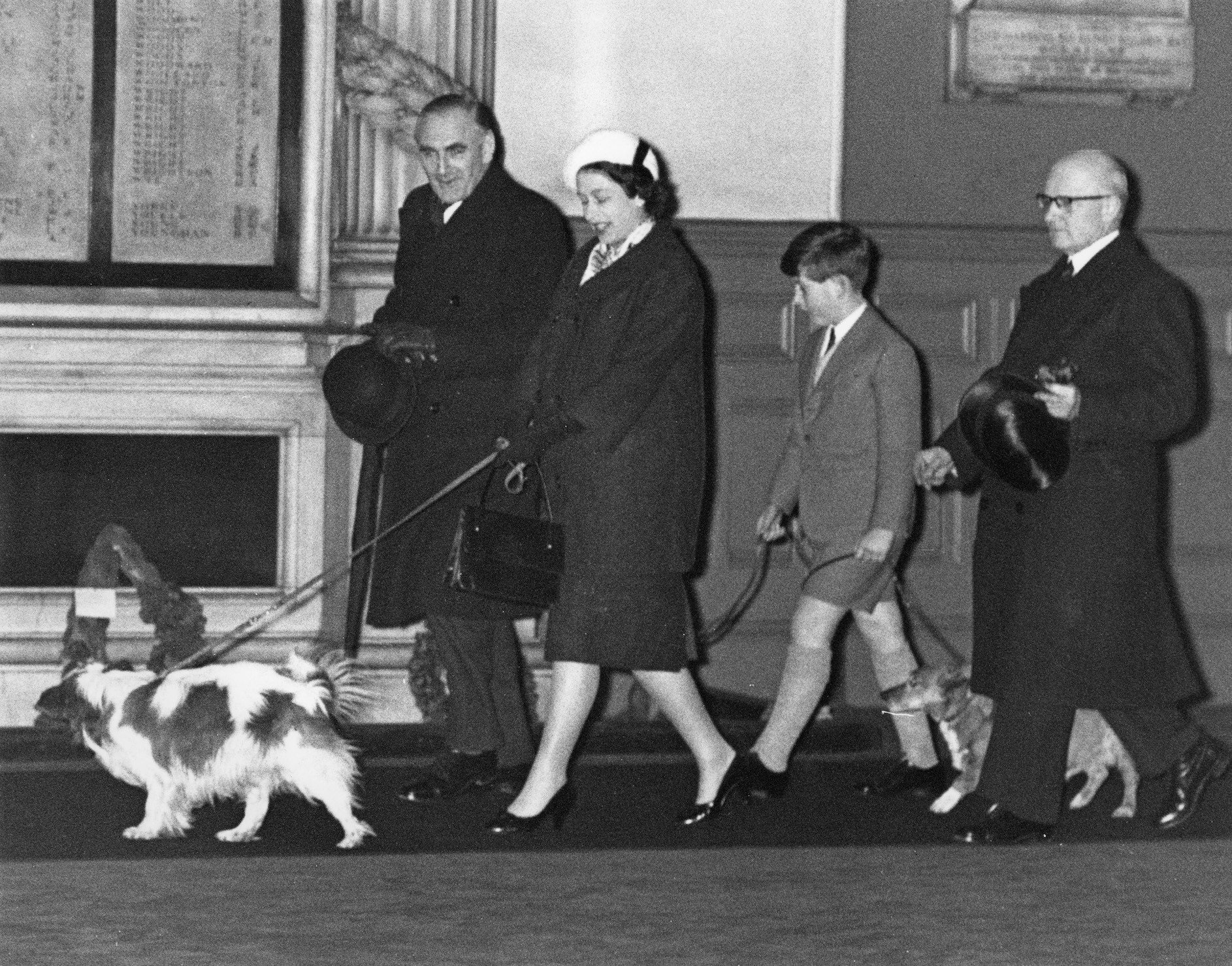 Queen Elizabeth II and Prince Charles walk through Liverpool Street Station in London with their dogs