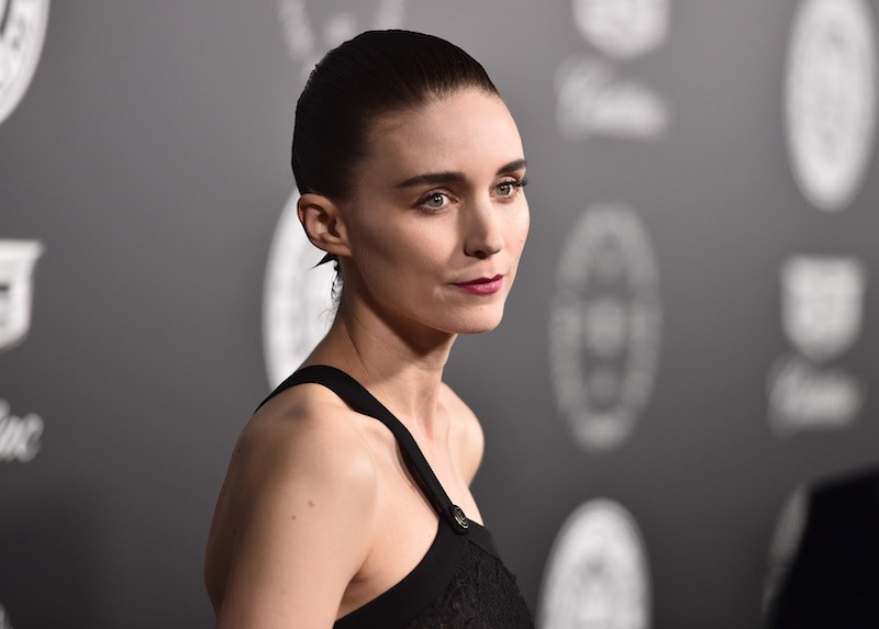 Rooney Mara poses on a red carpet in a black dress. Rooney Mara poses on a red carpet in a black dress.