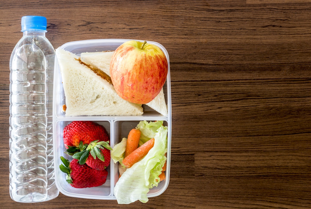 Lunch box with vegetables and slice of bread for a healthy school lunch on wooden table