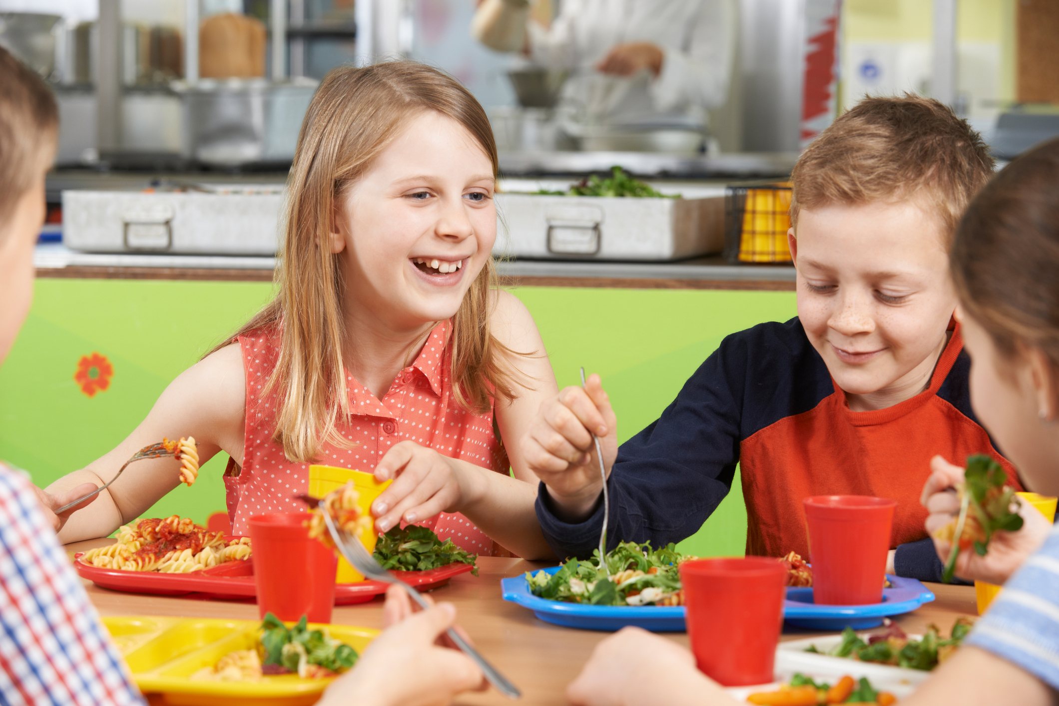 Group Of Pupils Sitting At Table In School Cafeteria Eating Lunch