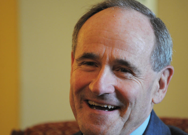 Jim Risch sits on a couch and smiles. 