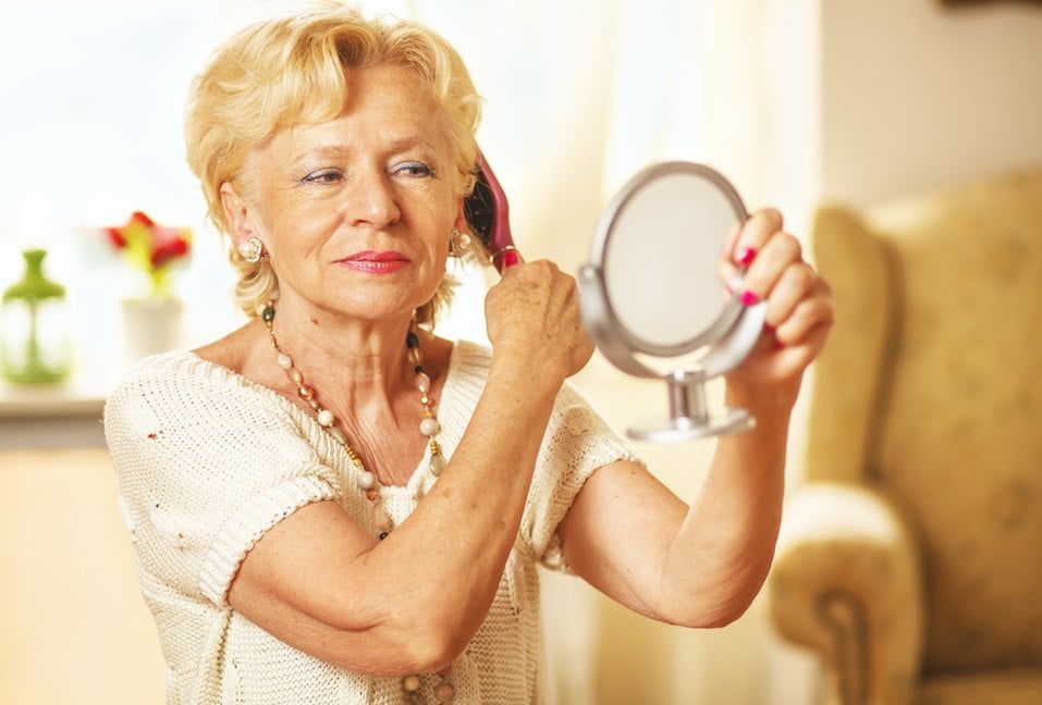 Smiling elderly woman comb hair and looked in the mirror