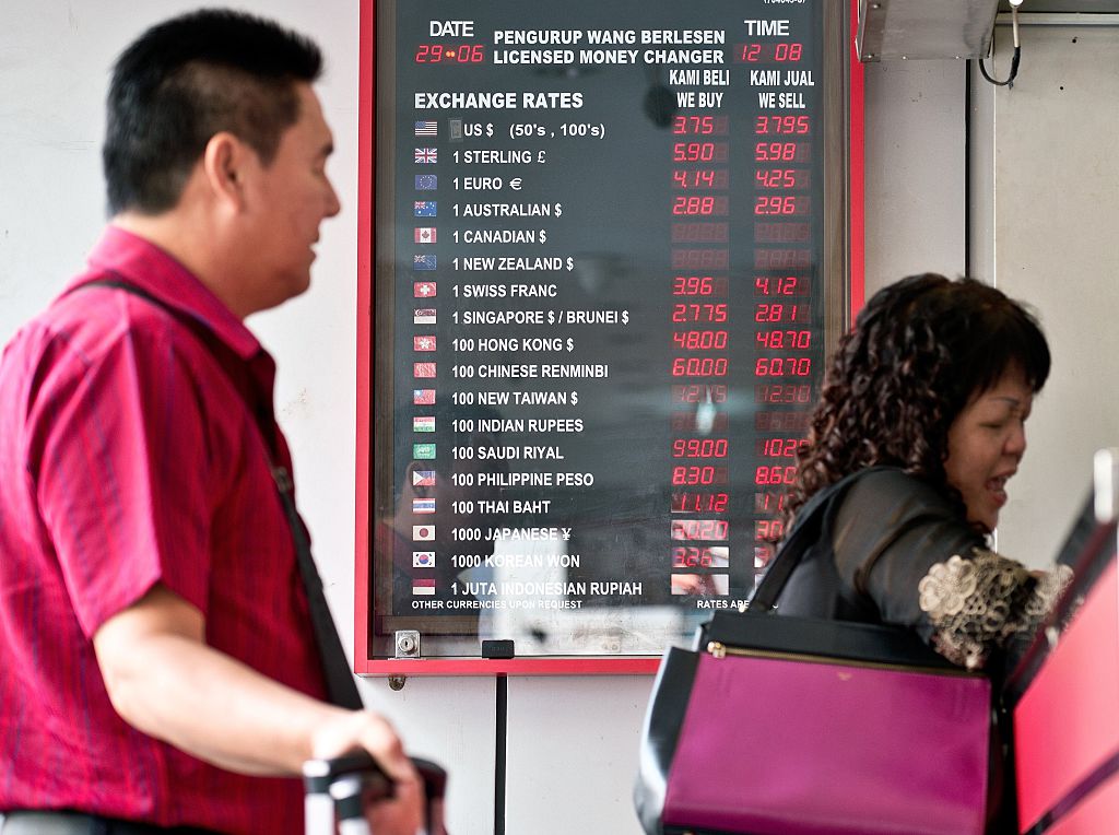 Tourists stand in front of a foreign currency exchange rate display board
