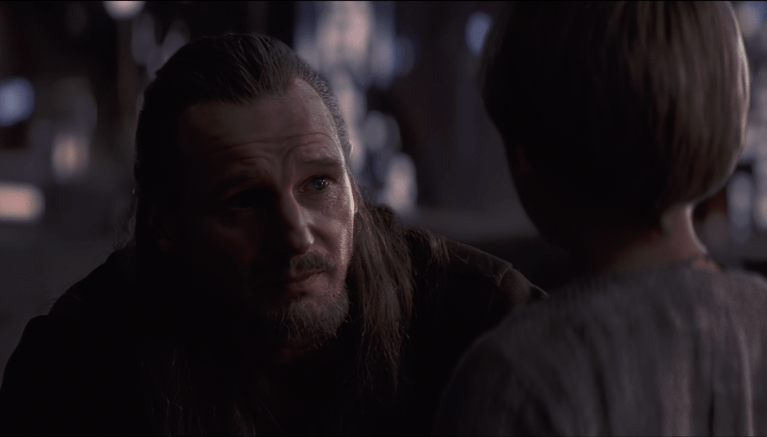 Qui-Gon crouches down as she speaks to young Anakin.
