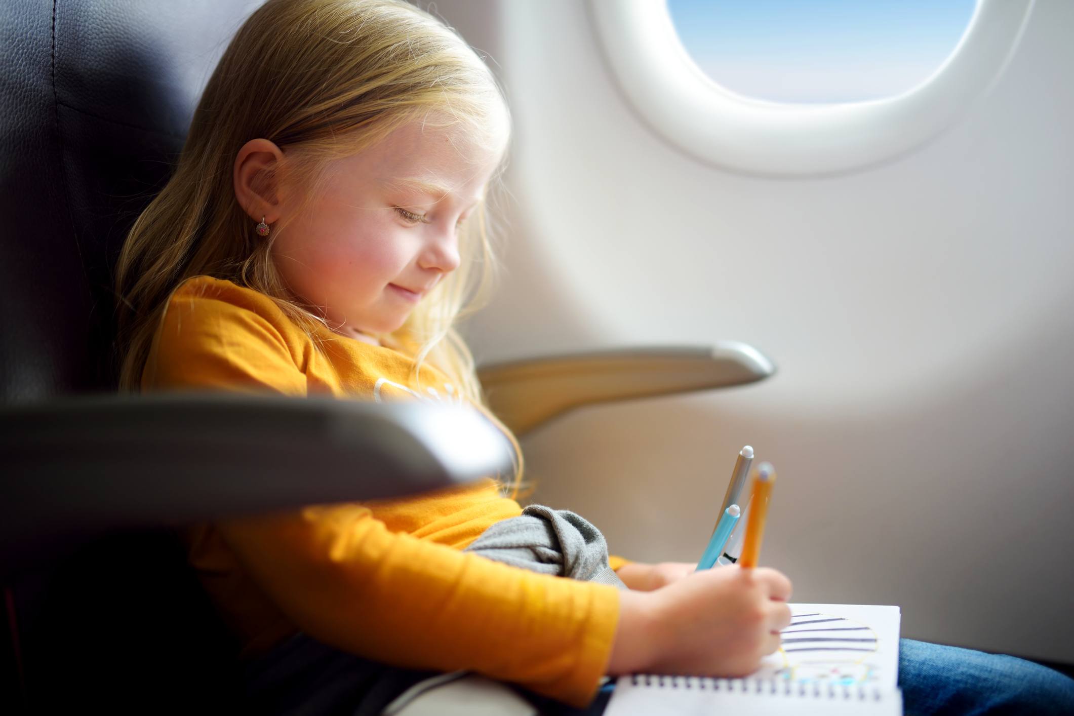 Adorable little girl traveling by an airplane. Child sitting by aircraft window and drawing or coloring a picture with felt-tip pens.