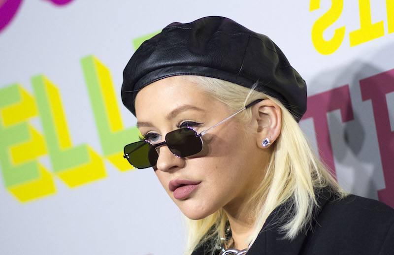 Christina Aguilera on a red carpet, wearing black sunglasses and a black beret. 