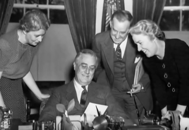 Franklin Delano Roosevelt holding a document and smiling with others around him Franklin Delano Roosevelt holding a document and smiling with others around him