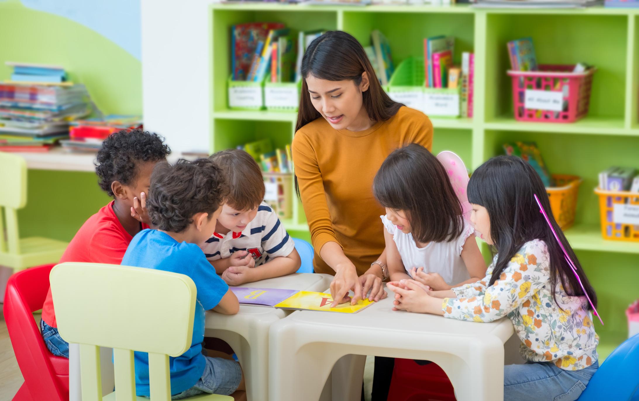 Asian female teacher teaching mixed race kids reading book in classroom,Kindergarten pre school concept.