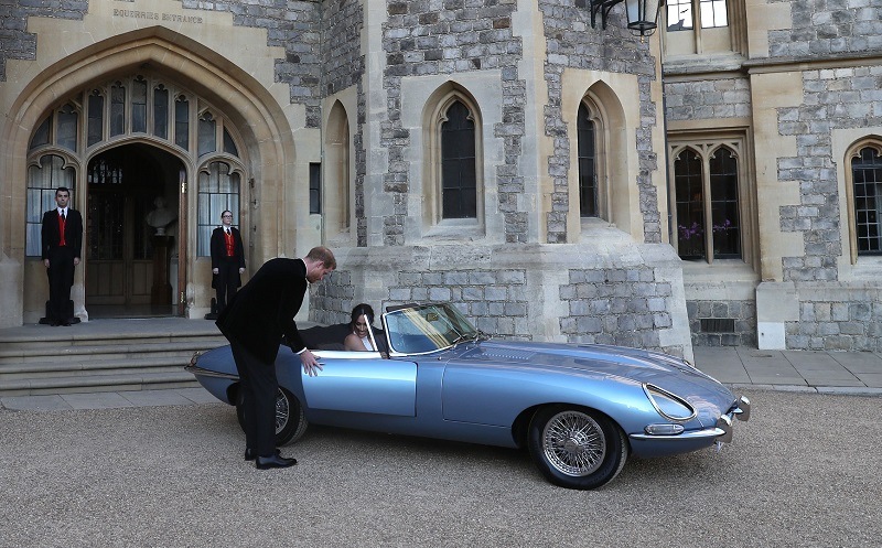 Britain's Prince Harry, Duke of Sussex, (L) opens the passenger door of an E-Type Jaguar car for his wife Meghan Markle, Duchess of Sussex, (R) as they leave Windsor Castle in Windsor on May 19, 2018 after their wedding to attend an evening reception at Frogmore House.