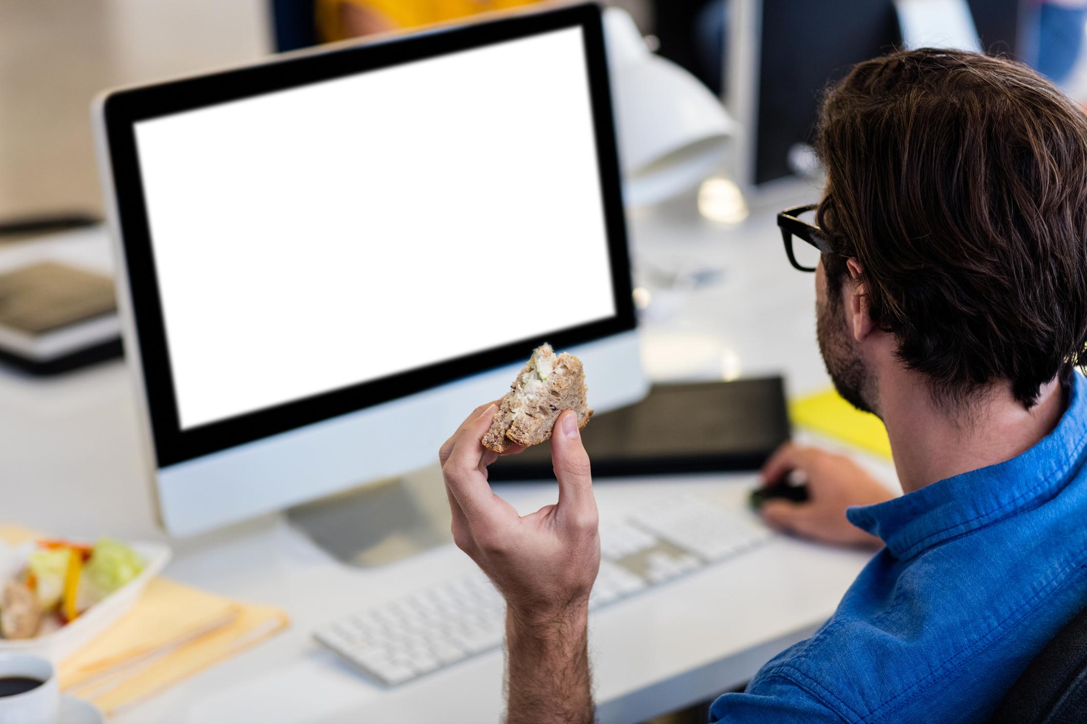 Casual businessman eating a sandwich in front of the computer