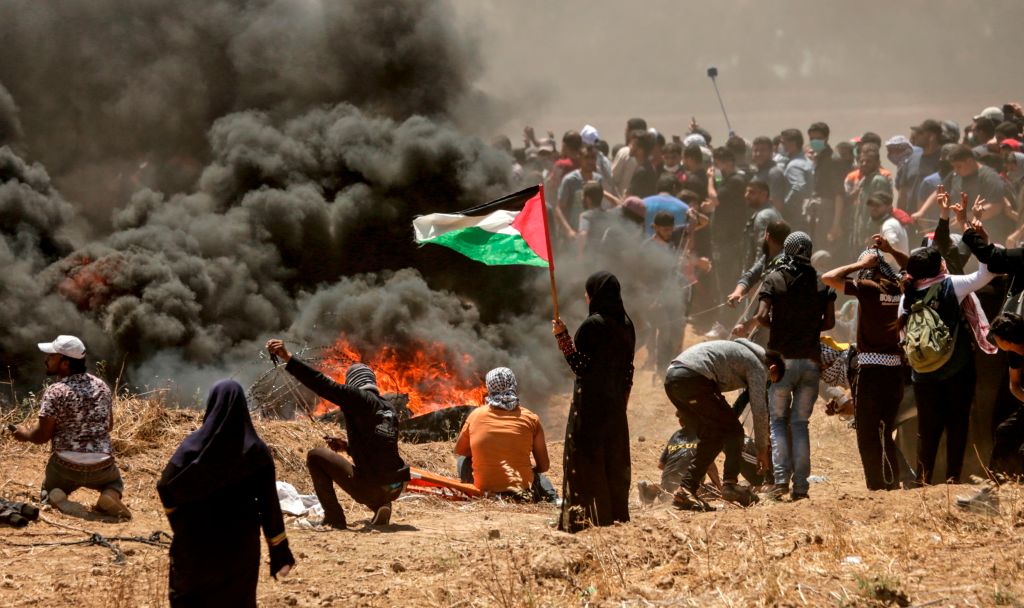 A Palestinian woman holding her national flag looks at clashes with Israeli forces