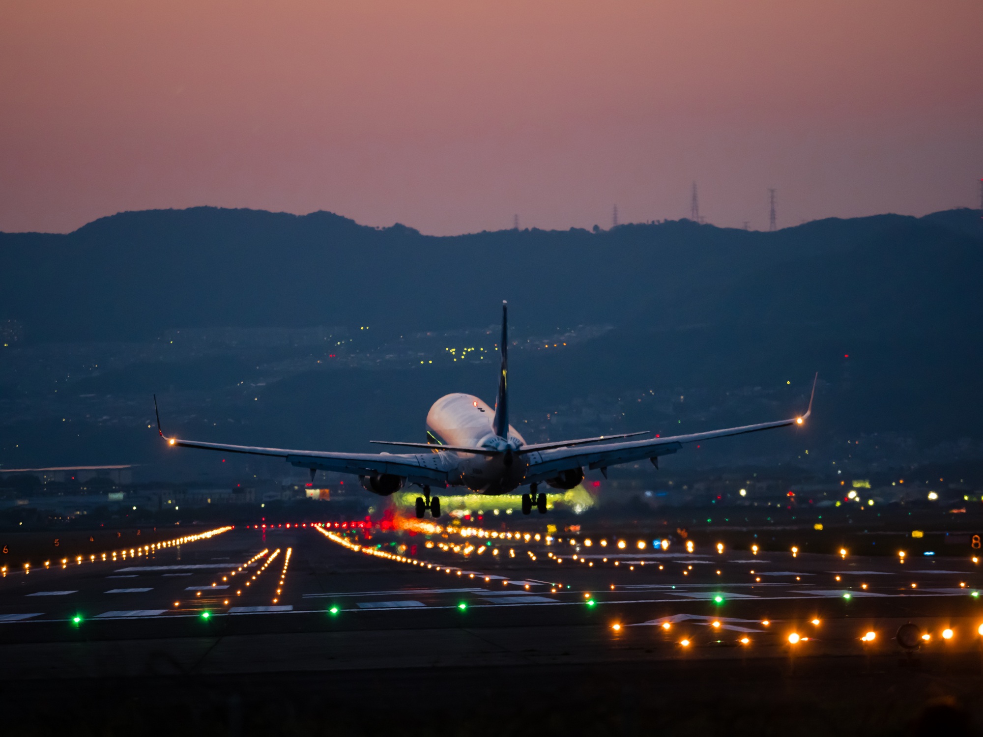 Plane landing on the runway at night with lights and a sunset