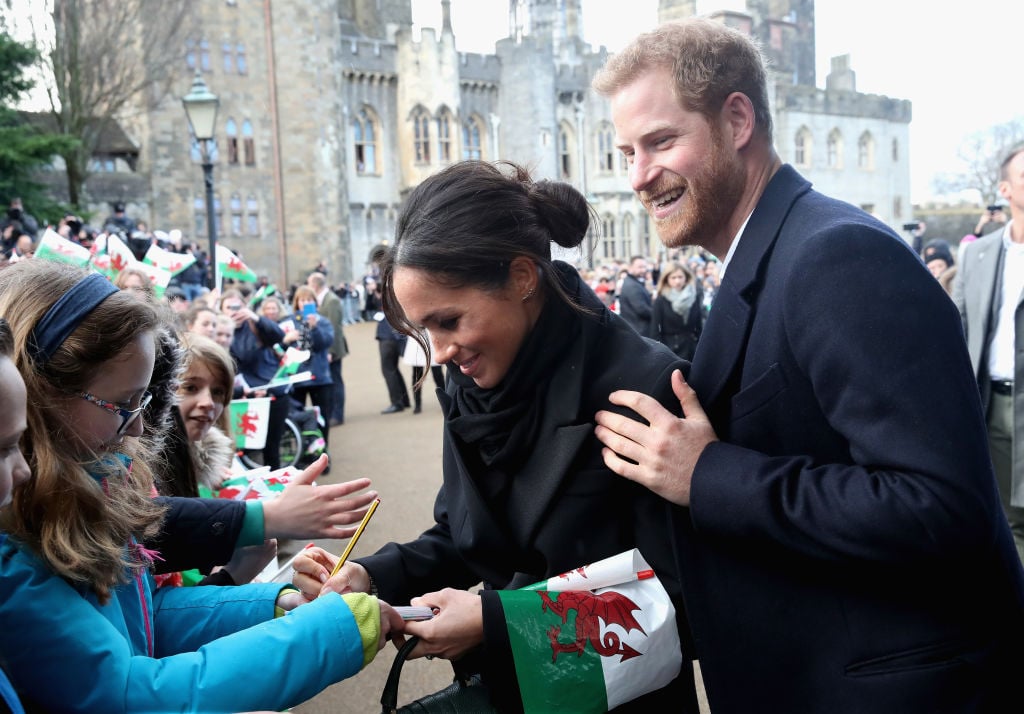 Meghan Markle writes a note for 10 year old Caitlin Clarke from Marlborough Primary School as Prince Harry looks on during a walkabout