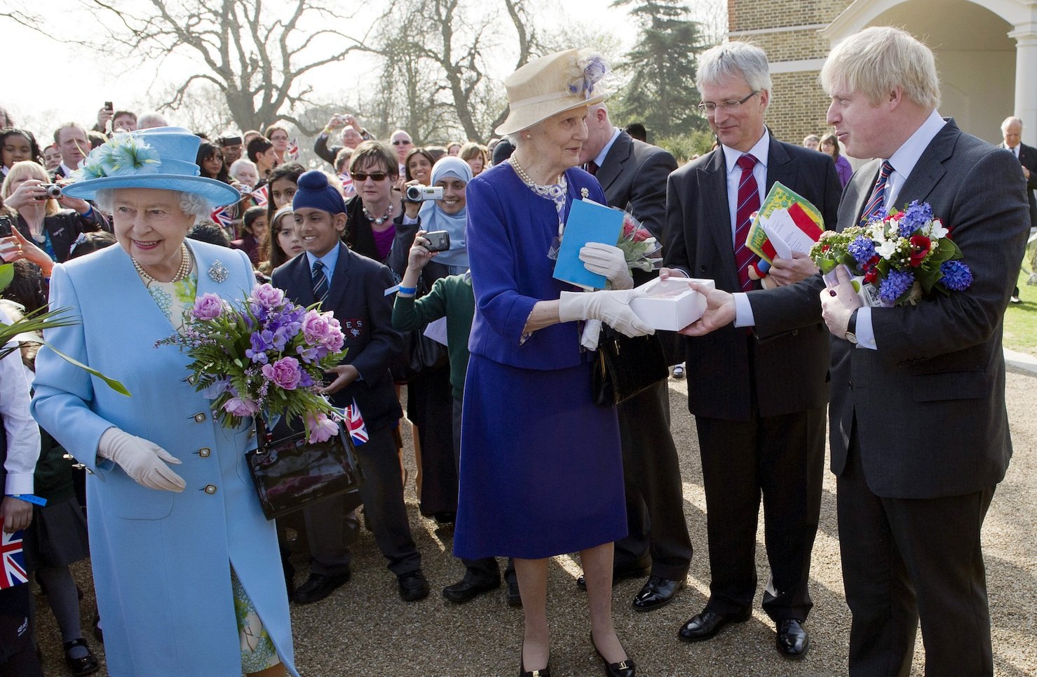 London Mayor Boris Johnson (R) and a lady-in-waiting (C) help Britain's Queen Elizabeth II (L) with her many gifts 
