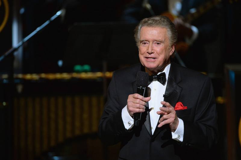 Regis Philbin speaking into a microphone while wearing a black tuxedo. Regis Philbin speaking into a microphone while wearing a black tuxedo.