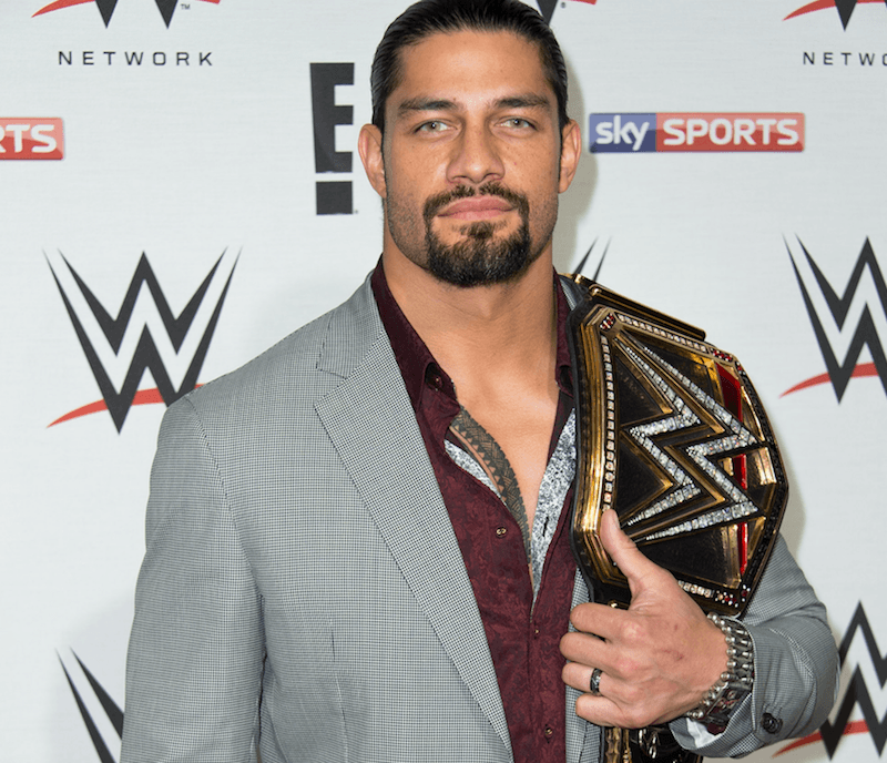 Roman Reigns posing on a red carpet with a wrestling belt. 