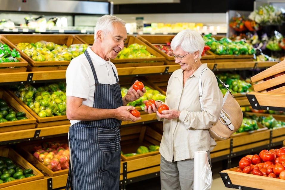 Senior customer and worker discussing vegetables in supermarket