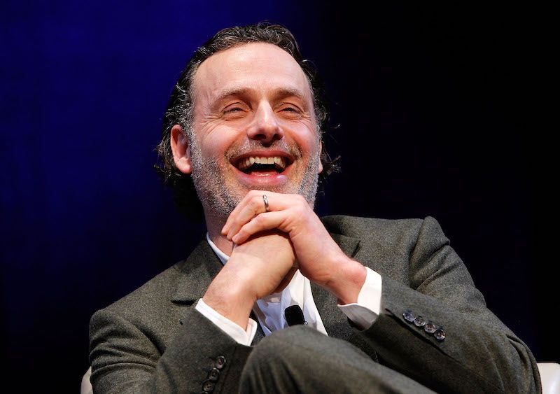 Andrew Lincoln laughing while siting on stage during a press event.