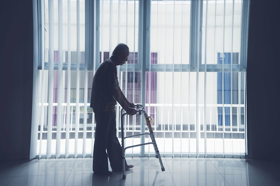 Elderly man walks with a walker near the window Elderly man walks with a walker near the window