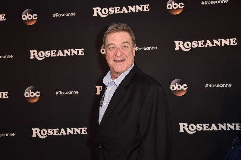 John Goodman wearing a black suit on a red carpet. John Goodman wearing a black suit on a red carpet.