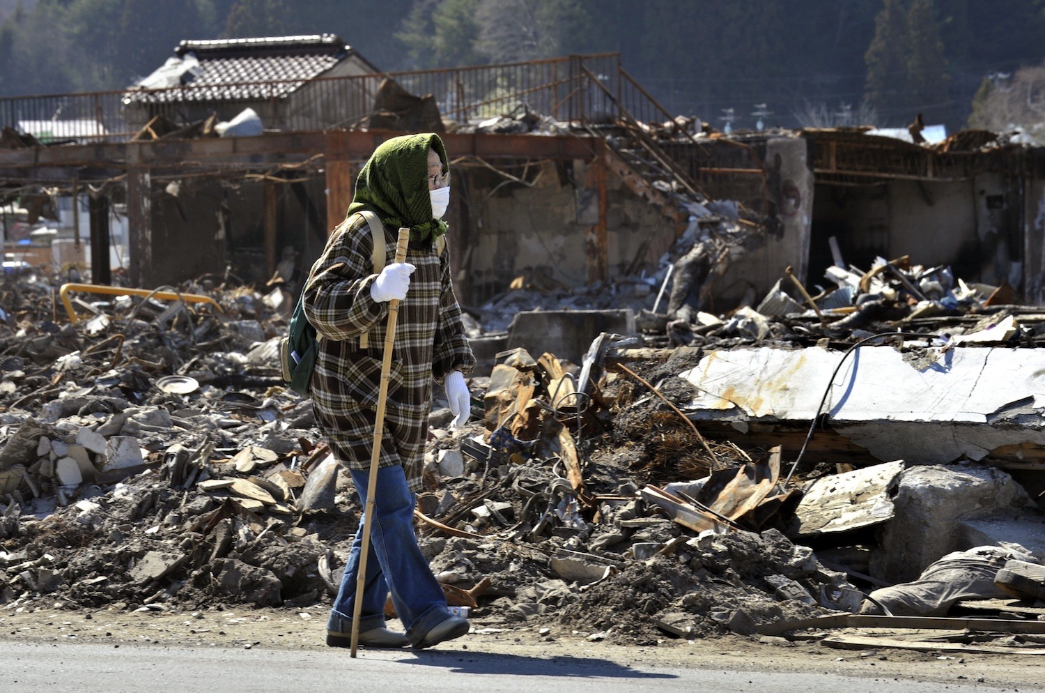 An elderly woman walks amongst tsunami debris
