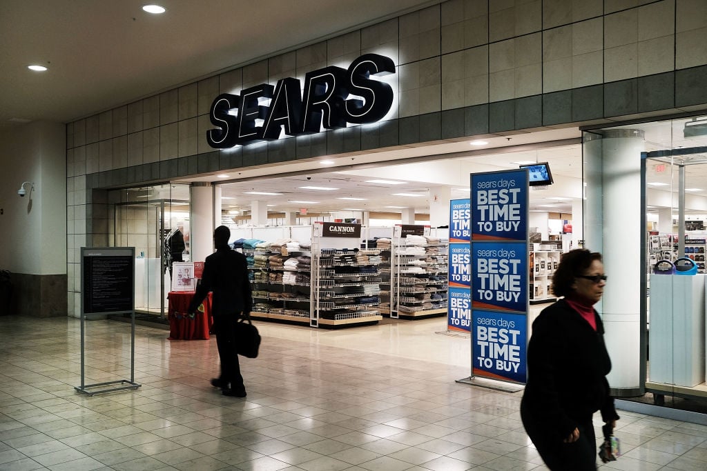 People walk by a Sears store in a nearly empty Westfield Meriden shopping mal