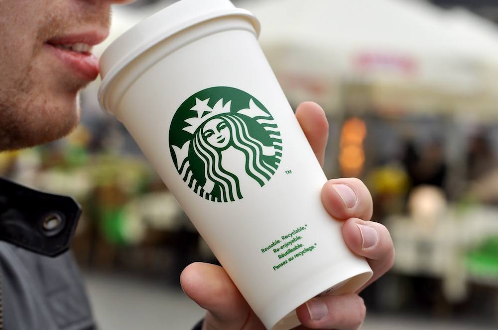 A man holds a hot beverage from Starbucks