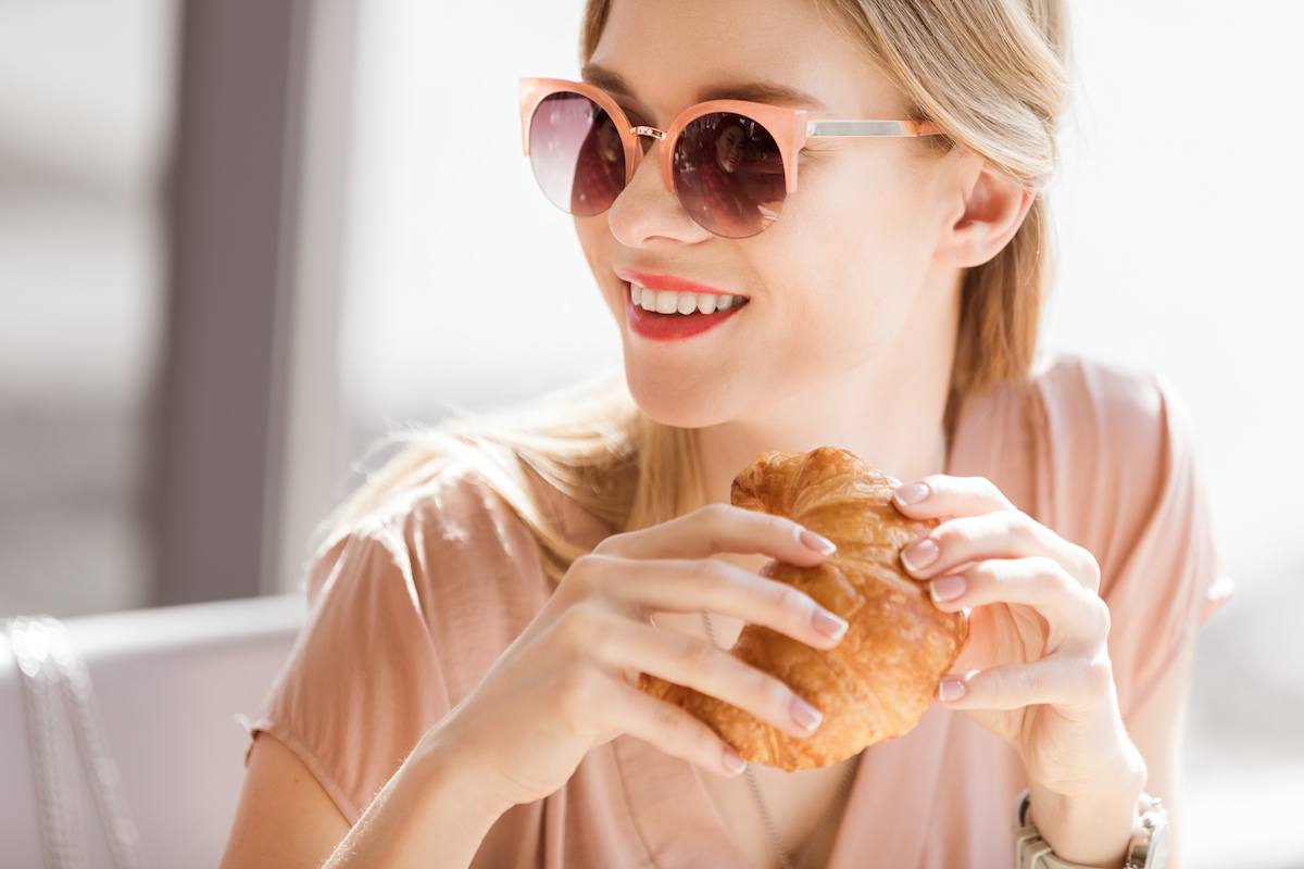 woman eating Young woman eating a croissant at a cafe
